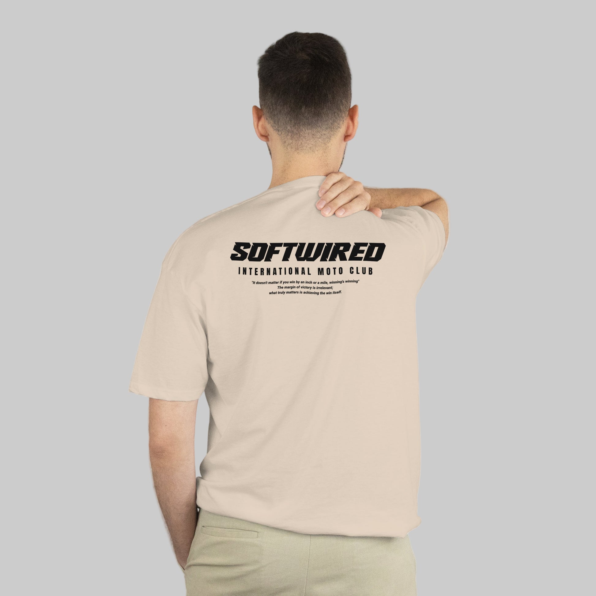 Man wearing a beige t-shirt with 'SOFTWIRED' logo on the back, standing against a white background