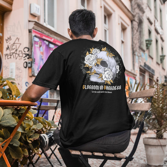 Person wearing a black t-shirt with a skull design and text, sitting on a bench in an urban setting.