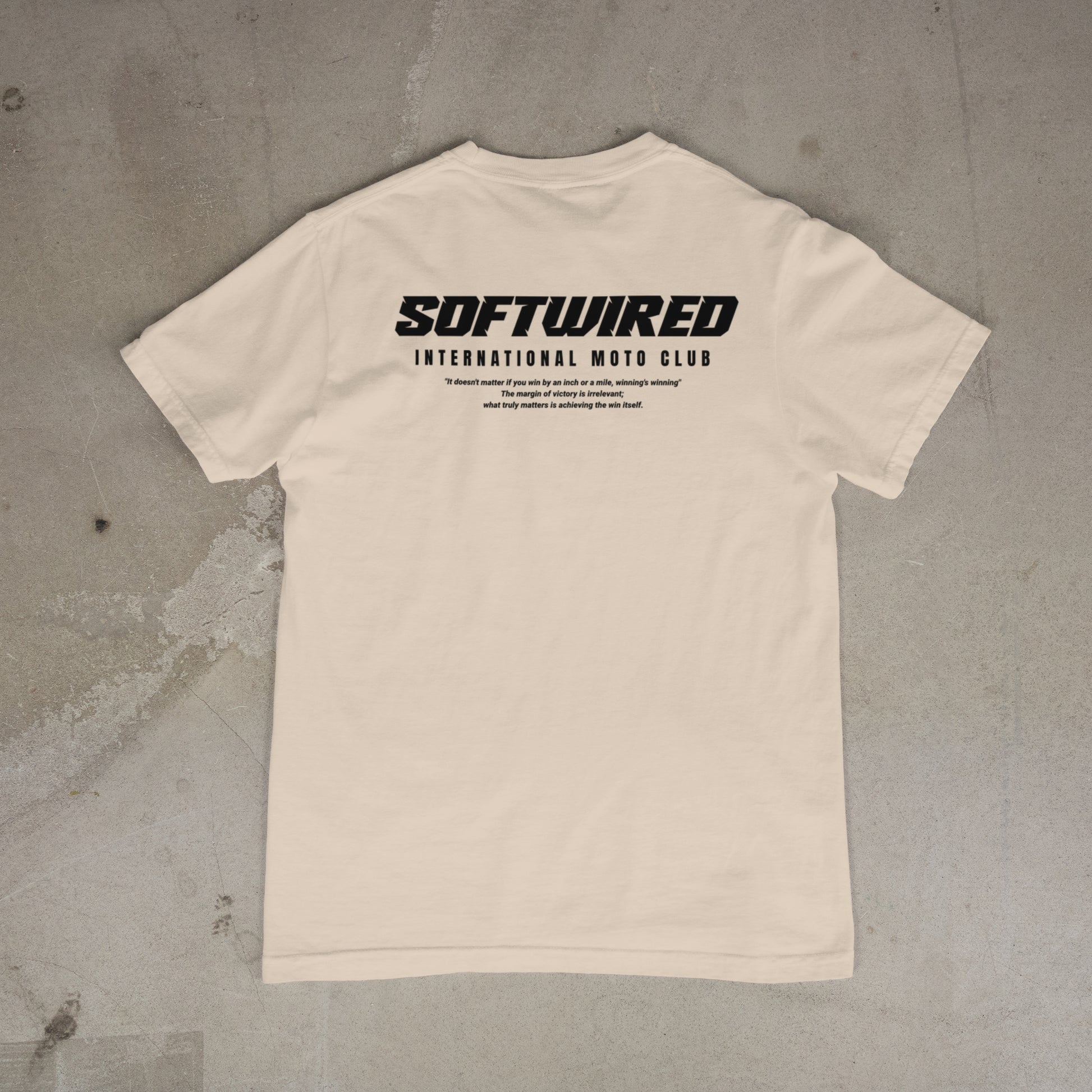 Beige t-shirt with 'SOFTWIRED' text on the back against a concrete background