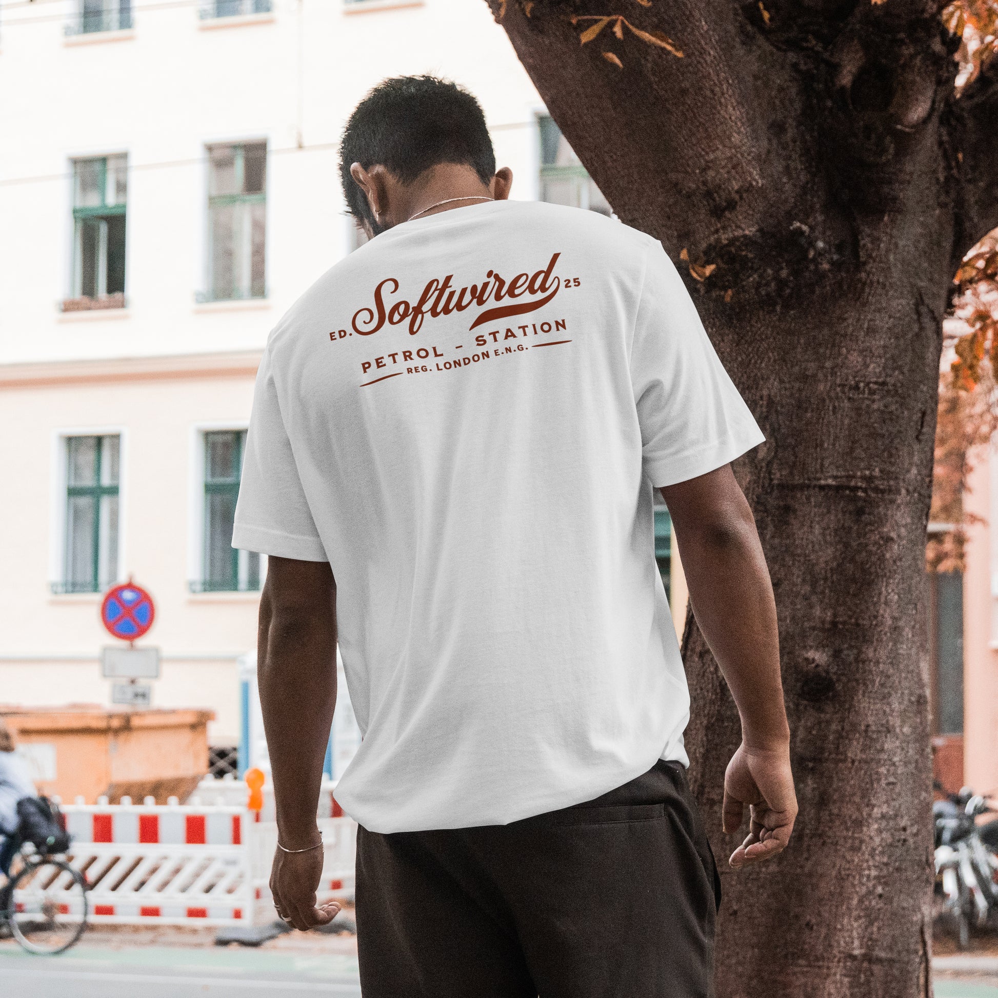 Person wearing a white t-shirt with 'Softwired' branding on the back, standing next to a tree in an urban setting.